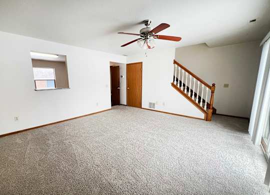 A room with a carpeted floor and a ceiling fan.