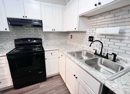 A black oven sits in a kitchen with white cabinets and a marble countertop.