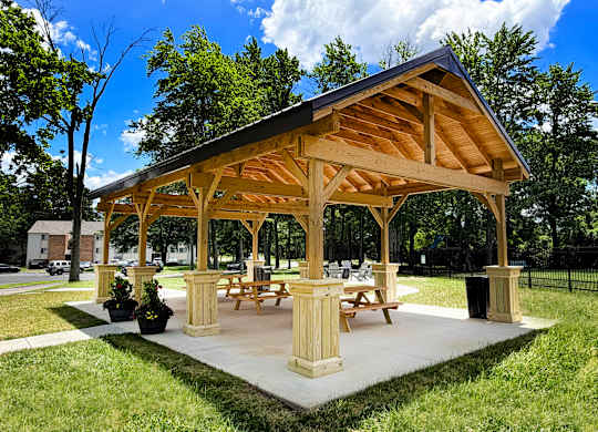A wooden pavilion with picnic tables is surrounded by green grass.
