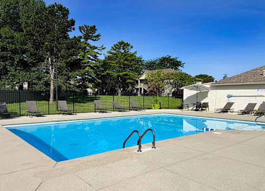 A swimming pool surrounded by a concrete patio and lounge chairs.