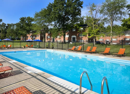 a swimming pool with orange chairs and a fence around it at Sharondale Woods Apartments, Cincinnati