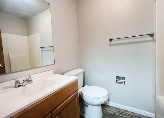 A white toilet sits in a bathroom next to a sink and a towel bar.