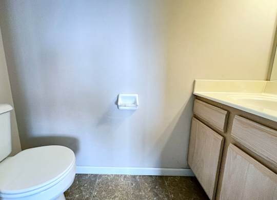 A white toilet sits next to a white wall and a white sink.