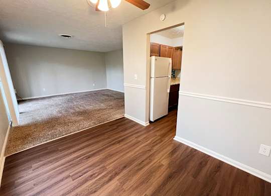 A room with a brown floor and a white fridge.