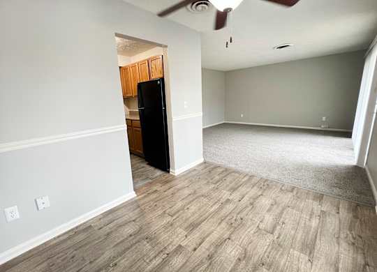 A room with a black fridge and wooden flooring.