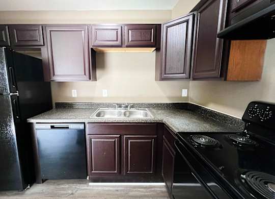 A kitchen with dark brown cabinets and black appliances.