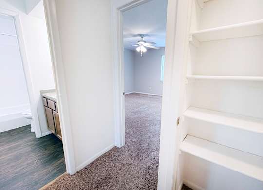 A white shelving unit is in a room with a carpeted floor and a ceiling fan.