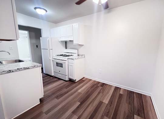 A kitchen with white appliances and wood flooring.
