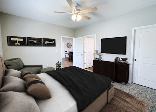 A bedroom with a bed, couch, and a television mounted on the wall.