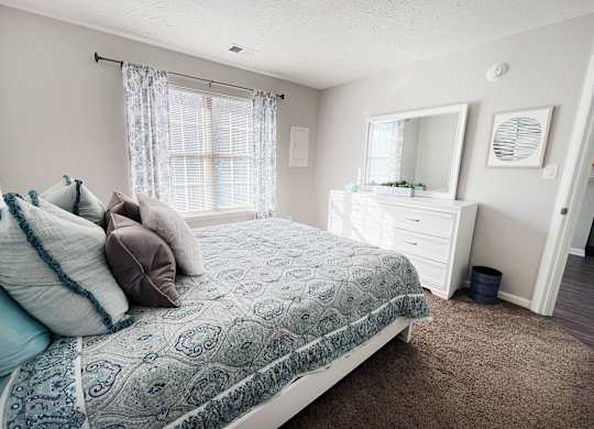 A bedroom with a bed, dresser, and window.