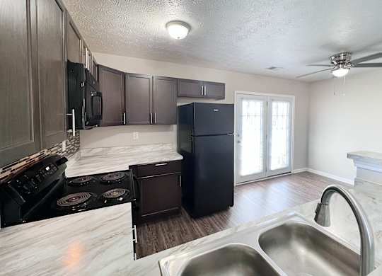 A kitchen with a black refrigerator and stove top oven.