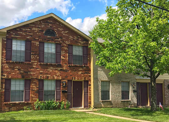 A red brick house with a tree in front.