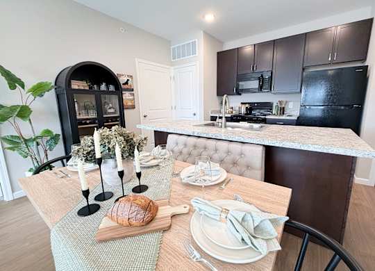 A dining table set with plates and cutlery is in front of a kitchen.