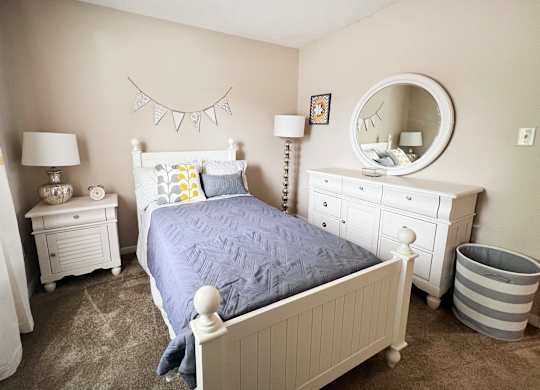 A bedroom with a white bed, dresser, and nightstand.