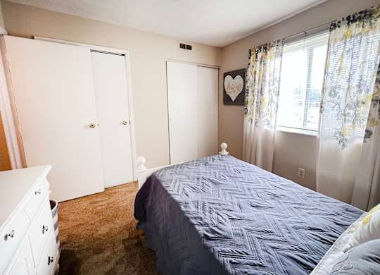 A bedroom with a bed, dresser, and window.