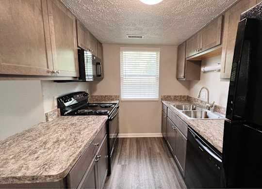 A kitchen with a black refrigerator, a stove, and a microwave.