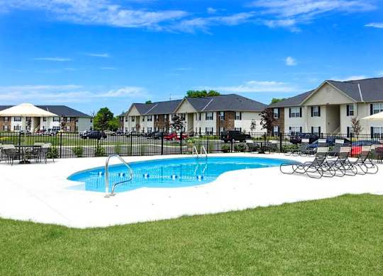 A swimming pool in a grassy area with chairs and umbrellas.