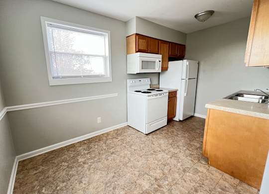 an empty kitchen with white appliances and a window