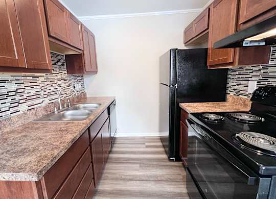 A kitchen with a black refrigerator and a granite countertop.
