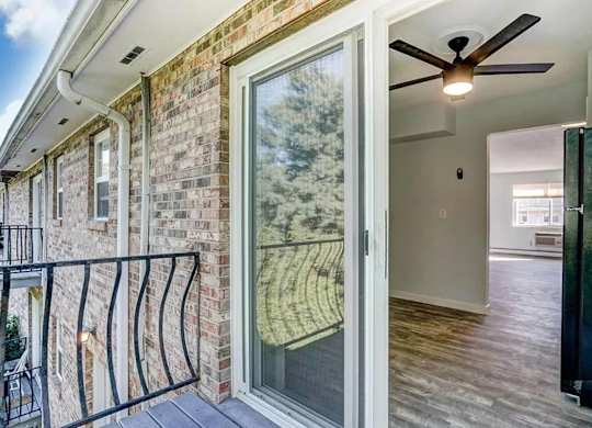 A balcony with a black railing and a glass door leading to a room with a ceiling fan.