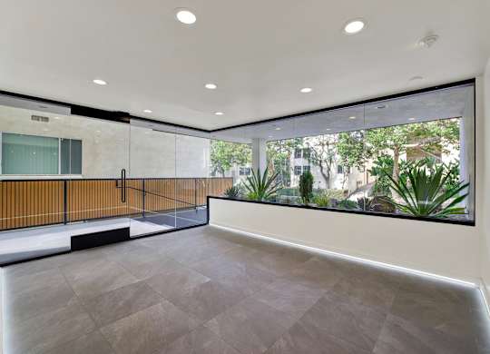 A spacious room with a grey floor and a large window overlooking a garden.