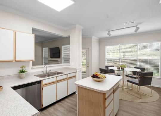An open kitchen with a stainless steel dishwasher, white cabinets, a kitchen island next to a dining area with large windows.