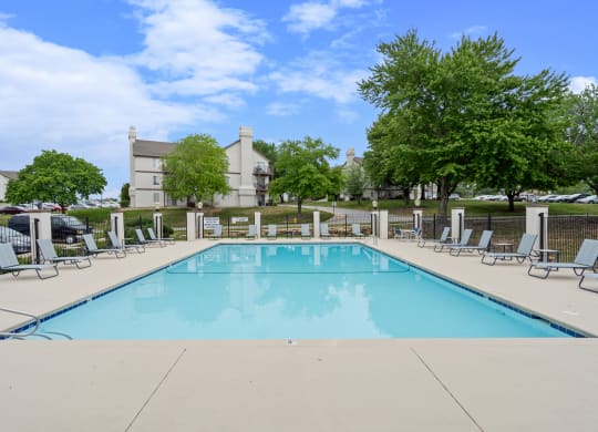 a swimming pool with chaise lounge chairs and trees in the background at Millcreek Woods Apartments, Kansas, 66061