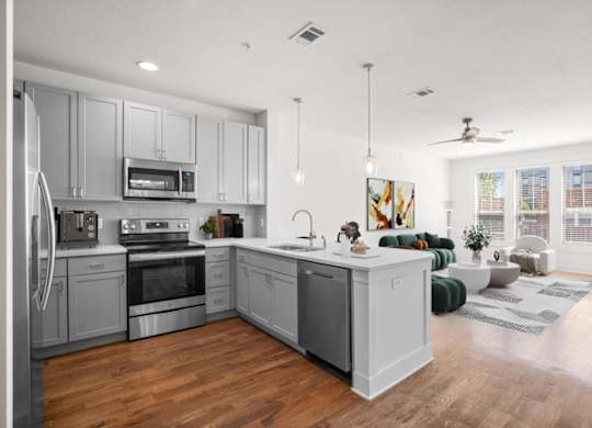 A large, open gourmet kitchen with stainless steel appliances including microwave and dishwasher, hardwood floors, and pendant lighting.