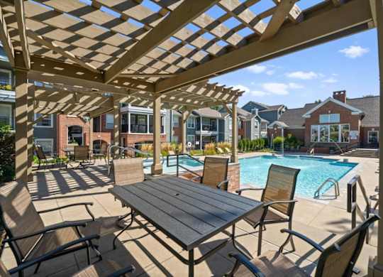 A wooden pergola over a table with chairs and a pool in the background at Somerset Oaks Apartment Homes, Olathe, 66062