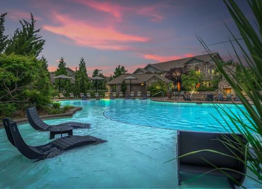 A pool with loungers and a house in the background during sunset.