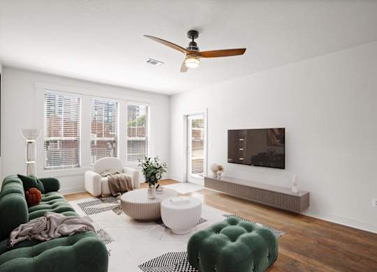 A living room with hardwood floors, a ceiling fan, and windows.