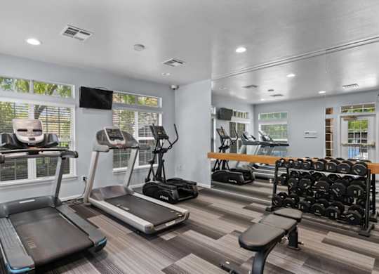 A gym with treadmills, elliptical machines, and dumbbells.at Crowne Chase Apartment Homes, Overland Park, KS, 66210