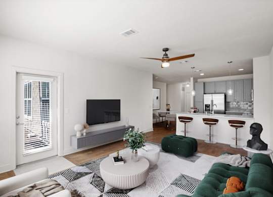 Living room with a ceiling fan, balcony entrance door, hardwood floors, and a modern kitchen in the background.