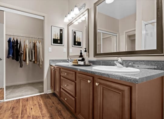 A bathroom with a double vanity sink, dark espresso cabinets and drawers, lots of counter space, large vanity mirrors with great lighting, and a large sliding glass door closet.