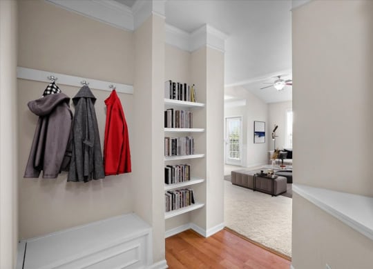 A mud room with shoe storage mud bench, coat hooks, a built-in book shelf, and hardwood floors.