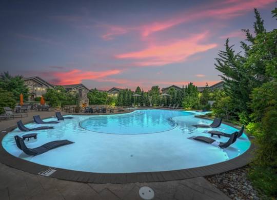 A round swimming pool surrounded by lounge chairs and trees.