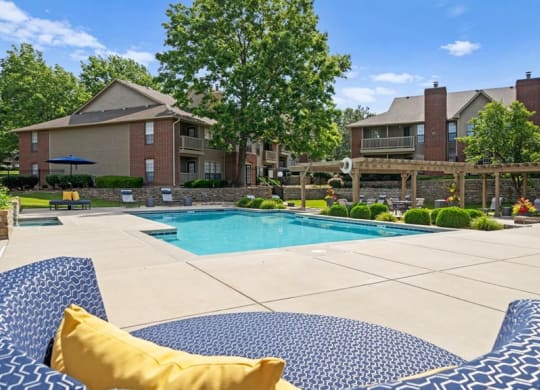 a swimming pool with blue and white chairs and a house in the background at Highland Park Apartment Homes, Overland Park