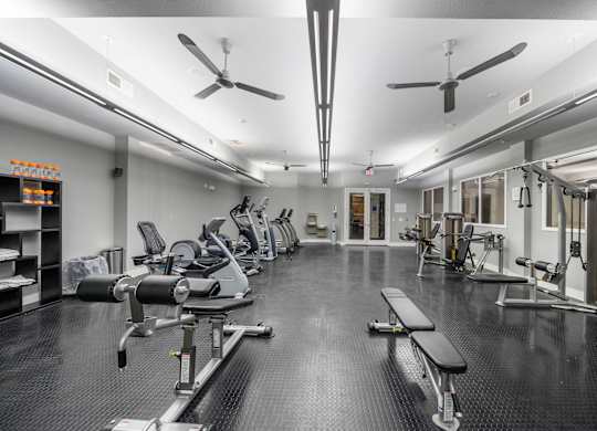 Fully-equipped gym at West 39th Street Apartments with workout benches, cable machines, cardio stations, and ceiling fans at West 39th Street Apartments, Kansas City, MO, 64111