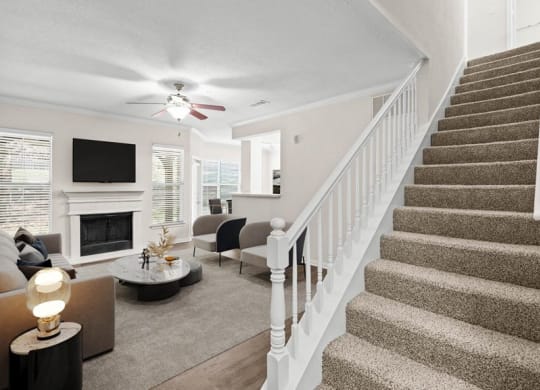 A living room with a fireplace, a ceiling fan, and a staircase.