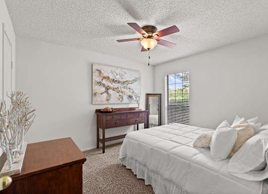 A bedroom with a bed, dresser, and a ceiling fan.