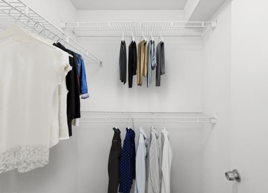 a walk in closet with white walls and a white metal shelf with clothes on it