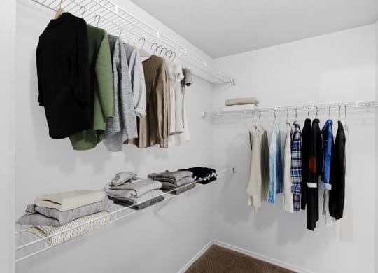 a walk in closet with white shelves and a white rod with clothes hanging on it