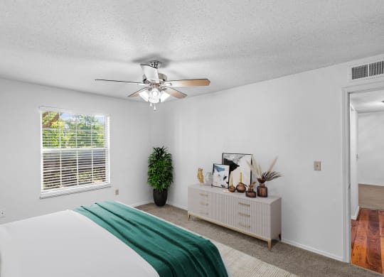a bedroom with a large white bed and a white dresser with a green blanket on itat Stonebriar Apartments, Kansas