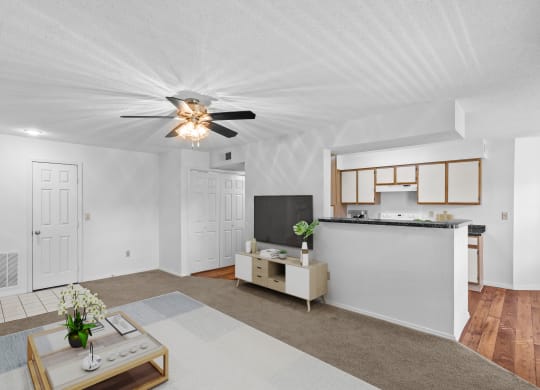 a living room with a ceiling fan and a kitchen in the backgroundat Stonebriar Apartments, Overland Park, KS
