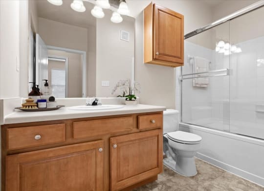 A bathroom with oak cabinets and drawers, a large vanity mirror with great lighting, and a garden soaking tub shower combo with a sliding glass door.