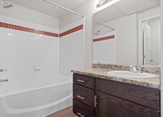 A secondary bathroom with a tub shower combo and a vanity with a large mirror and storage cabinets under the sink.