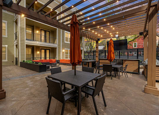 Outdoor lounge at West 39th Street Apartments with pergola, string lights, dining tables, and mounted TV at West 39th Street Apartments, Missouri