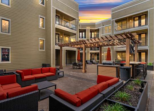 Sunset view of the outdoor courtyard at West 39th Street Apartments with red cushioned lounge seating, pergola, and grilling station at West 39th Street Apartments, Kansas City, MO
