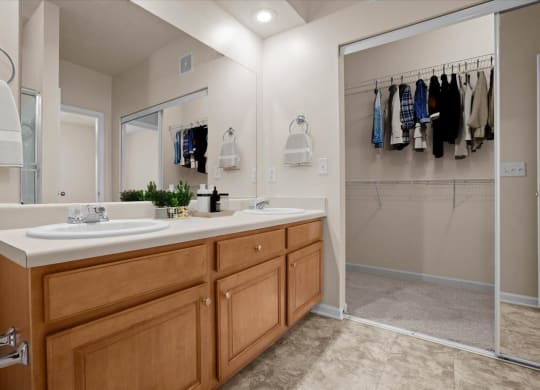 A bathroom with double vanity sinks, oak cabinets and drawers, a large vanity mirror, and a sliding glass door closet.