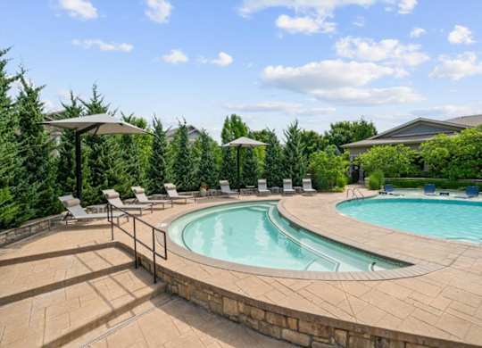 A large outdoor swimming pool surrounded by a stone wall and lounge chairs.